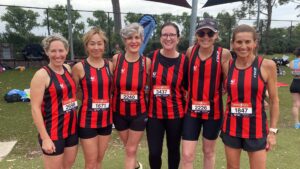 Six female athletes in red and black uniforms smile facing the camera